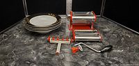 Remy Olivier Scarlet pasta machine with hand crank and pasta cutter attachment next to 4 decorative bowls on marble surface