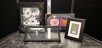 Four picture frames arranged on a table - three wall frames (two large, one medium) with protective corners, and one black tabletop frame standing up.