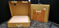 Box of a collapsible storage ottoman opened to show the padded cushioned top inside and the box with the Kvell branding.