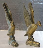 Front view of two brass bird figurines with wings raised, showing detailing and base structure.