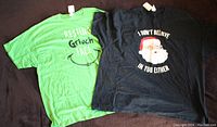Two men's Christmas t-shirts laid flat, one green with 'Resting Grinch Face' text and one black with Santa graphic and text 'I Don't Believe In You Either'.