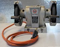 Front angle photo showing the bench grinder with power cord coiled beside it, displaying the overall condition and setup.