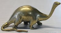 Side view of the brass dinosaur figurine, showing the body, neck, and tail shape.