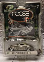 Front view of unopened Foose Design Series Impression die-cast model car in original packaging with clear plastic showing silver car and black card with branding.