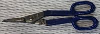 Mastercraft tin snips showing full length and blade shape, blue plastic-covered handles, placed on lined background.