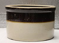 Side view of the old stoneware crock showing dark brown glazed top band and off-white lower body.