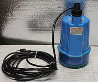 Full view of the blue Chicago submersible electric water pump with attached long black power cord and plug, sitting on a surface.