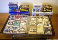 Overview of entire collection: binder open with baseball cards displayed inside, two 1987 Fleer tins and two 1988 Fleer tins stacked behind, two boxes of card holders on top of tins.