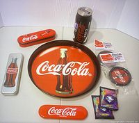 Full view of Coca-Cola collection showing tray, coasters, pencil cases, water bottle and two unopened packs of bottle caps in original condition.