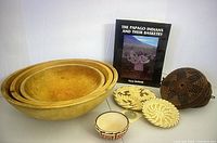 Photo showing three large nested wooden bowls, a small ornate bowl, three handmade baskets, and a book on Papago Indian basketry.
