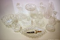 Collection of clear crystal glass items including decanters, vase, candy dish, bowls, decorative plate and dagger on a glass tray.