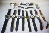 Photo showing 12 assorted wristwatches laid out flat, showcasing variety in band materials, dial styles, and colors.