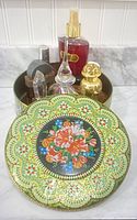 Ornate tin container with floral mosaic pattern and various perfume bottles inside