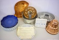 Complete assortment of vintage baking pans and molds including copper Jell-O molds, ceramic tart tins, aluminum tube pan, Pampered Chef flan pan, and tart pan with instructions.