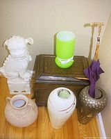 Photo showing the white ceramic Chinese dog or dragon statue, ornate metal box, green and white ceramic lantern, two decorative vases, and purple umbrella in dark vase.