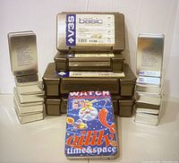 Photo showing 10 small metal fishing kit tins stacked on each side and 4 brown plastic tackle boxes stacked in the middle.