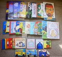 Full view of 34 assorted hardcover children's books laid out on carpet, showing front covers and spines, colorful illustrations, various titles.