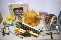 Photo showing entire kitchen supplies lot with vintage meat grinder, assorted cutters, decorative ceramic covered dish, knives, and boxed glass plate.