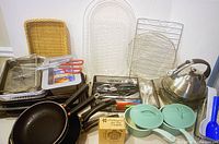 View of full kitchen tools lot including skillets with lids, kettle, trays, timers, utensils, plastic dishes, and wicker basket.