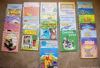 Photo showing 26 Little Golden Books laid out in three neat rows on a carpet, with colorful covers featuring classic children's story characters such as Dumbo, Winnie-the-Pooh, and Donald Duck.