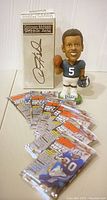 Photo showing a Donovan McNabb bobblehead in Eagles uniform with helmet and football, standing on oval base labeled 'Eagles'. Also visible are seven sealed 1997 Topps NFL football card packs stacked beside.