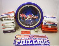 Full view of all items including 13 rally towels stacked, a large round Phillies clock, a Phillies license plate, a phone card holder, and a Fanatics figurine.