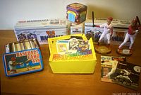 Overview of the lot showing three 1988 Fleer baseball card tins, yellow box with 1989 baseball cards, and two Phillies bobbleheads on wooden bases.