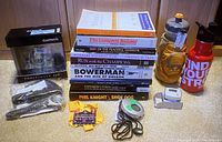 Lot of running accessories including watches, books, step counter, and water bottles on wood floor.