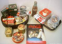 Full collection showing tins, trays, round and square coasters, postcards, Coca-Cola history book, and bottle opener, displaying vintage Coca-Cola branding and memorabilia.