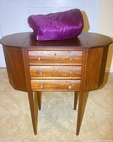Full front view of antique sewing table with purple fabric bag containing yarn on top.