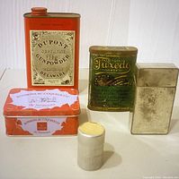 Five vintage tins displayed together showing varied sizes and labels, highlighting the gunpowder container, tobacco tin, bonbons tin, a small metal plain tin, and a cylindrical DuPont film tin.