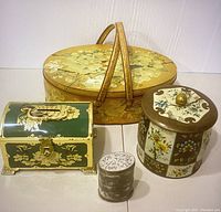 Photo showcasing entire lot of four vintage tins including picnic basket tin, ornate treasure chest tin, sugar tin, and floral panel tin.