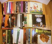 View of 40 vinyl record albums featuring various musical soundtracks including Mary Poppins, The Sound of Music, and Saturday Night Fever spread out on a wooden floor.