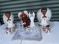 Wide view of the collection showing large praying angel figurines, Christmas choir angel figurines, crystal angels including a large cross, plastic placemats, and cloth.