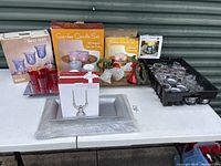 Overview of all items on table showing various boxed candle holder sets, loose votive holders, red votive holders on silver tray, a Mikasa crystal candleholder box and silver placemats.