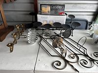 Pair of metal wall candleholders, LED candle set box, and glass votive holders arranged on a table.