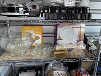 Photo shows vintage clear glass punch bowl with floral etching, matching punch cups, gold serving tray, decorative napkin rings, and garden candle set on a metal shelf.