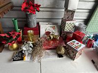 Overview of lot showing decorative Christmas-themed empty boxes of varying sizes with festive prints in red, white, and green, multiple mini vases including gold and green, several red fabric poinsettias in pots, gold glittery ornaments and berry branches, and rolls of tissue paper.