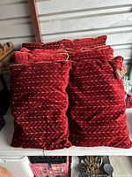 Eight red velvet plush pillows stacked together showing the front pattern and texture.