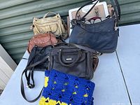 Overview of six handbags stacked together on a bench including a brightly colored crochet piece.