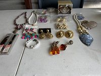 Assortment of various clip-on and pierced earrings, bracelets, necklaces, buttons, and watch bands displayed on a table.
