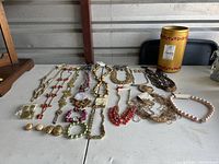 Wide view of jewelry lot including necklaces, earrings, bracelets, and rings, arranged on a white surface.