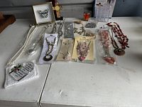 Wide view of assorted jewelry pieces including necklaces, pendent, beads; Todd Oldham Parfum box; butterfly art piece; lipstick organizer.