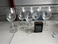 Nine large clear glass wine glasses arranged on a white table, approximately nine inches tall.
