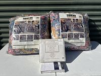 Two Twin Victorian Rose comforter sets in original packaging and one packaged King size Egyptian cotton sheet set with pillowcases on a white table in front of a storage door.