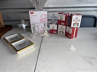Wide view of all items including Lang candy dishes, Mikasa boxes, loose crystal figurines, and framed pictures on white table