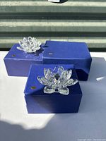 Three clear crystal lotus flower candleholders placed on blue boxes under sunlight.