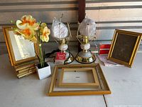 Full view of two touch me lamps with faux floral bulbs and five gold picture frames of various sizes laid out on table
