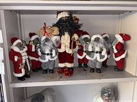 Shelf with 11 varied Santa Claus figurines in red and gray outfits, arranged standing side by side