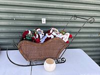 Large wood sleigh with woven sides filled with multiple Santa Claus figurines and a cream ceramic vase on table